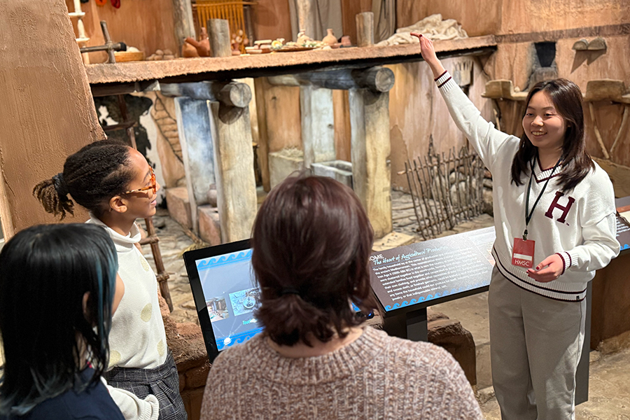 student guides visitors in front of house replica.