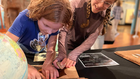 two kids cut hide with a stone tool in the gallery.