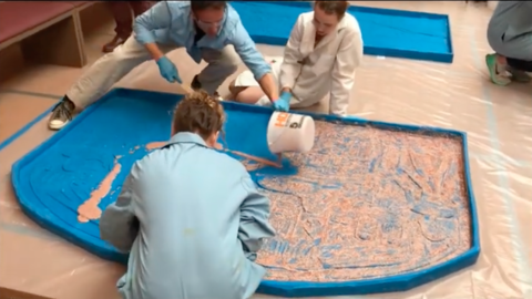3 people distribute resin in a silicone mold of the dream stela.