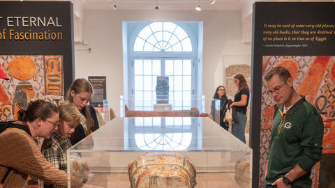 visitors gather around mummy coffin.