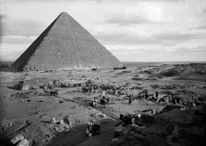 A vast landscape with the Khufu pyramid jutting out of the horizon with people busily at work on the base.