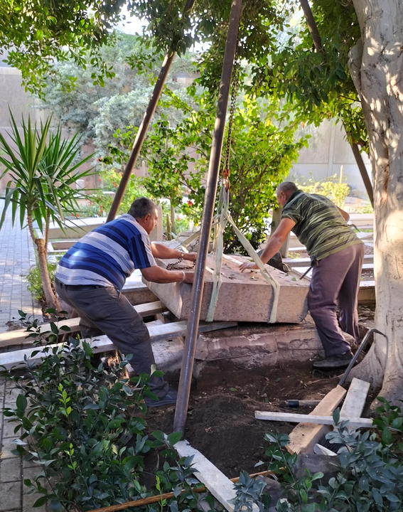 Two men carefully raising a tombstone amongst greenery.