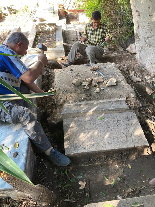 Two men carefully chipping away at the stone under the tombstone.