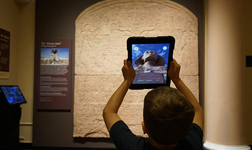 Child holding up an IPad experiencing a augmented reality of the sphinx.