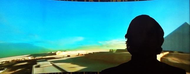 Man looking at a screen with a digital recreation of the area around giza and a pyramid.