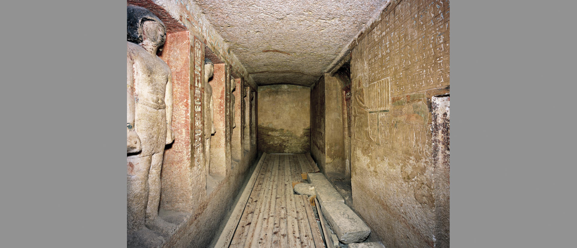 view down narrow chapel with carved figures on one side and hieroglyphs on the other.