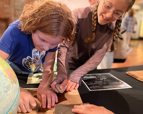 two kids cut hide with a stone tool in the gallery.